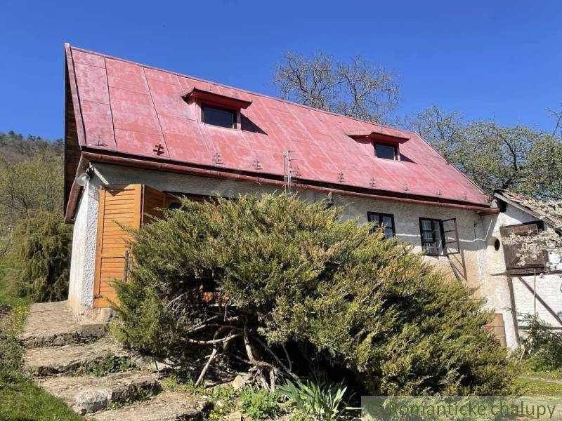 Chata v Rožňavě s červenou střechou, obklopená bujnou zelení a jasnou oblohou.