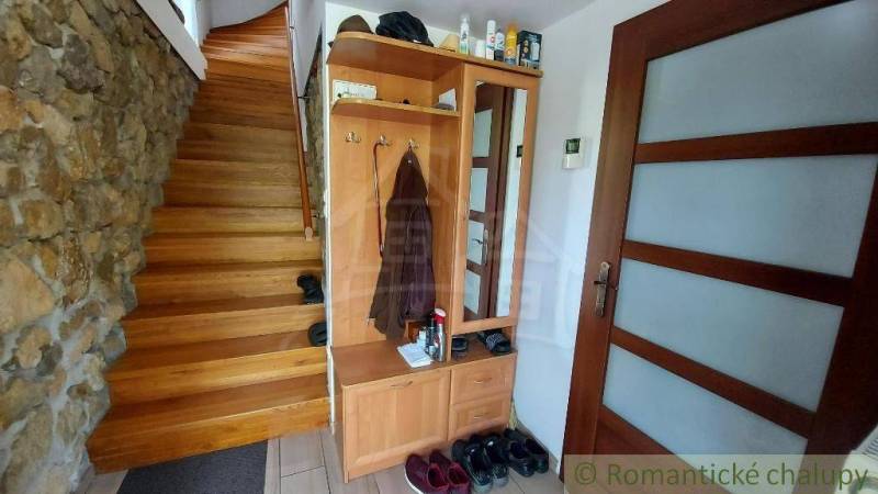 Interiér rodinného domu s dřevěným schodištěm, skříní a kamennou stěnou.