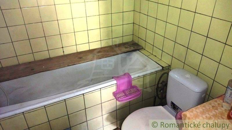 Koupelna v rodinném domě s vanou a toaletou, obklopená žlutými kachličkami.