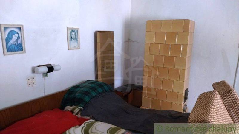 Pokoj v rodinném domě s kachlovými kamny, postelí a nástěnnými obrázky.