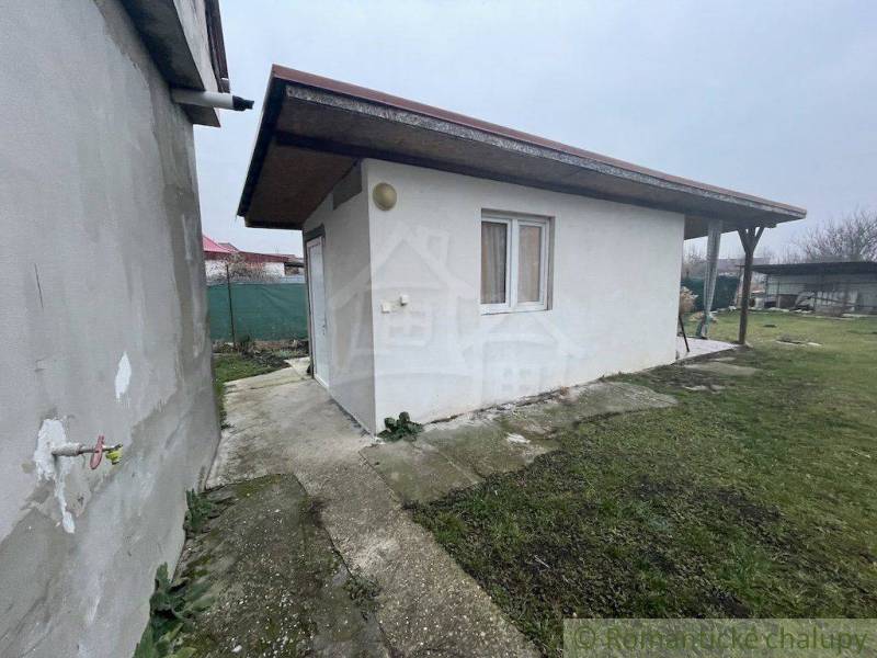 Zahradní altán u rodinného domu na zpevněné ploše s trávníkem a oplocením.