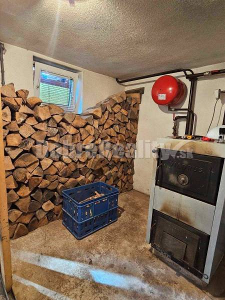 Kotolna rodinného domu s dřevem, kotlem a modrou přepravkou na podlaze.