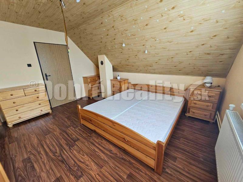 Ložnice v podkroví rodinného domu s dřevěným nábytkem a šikmým stropem.