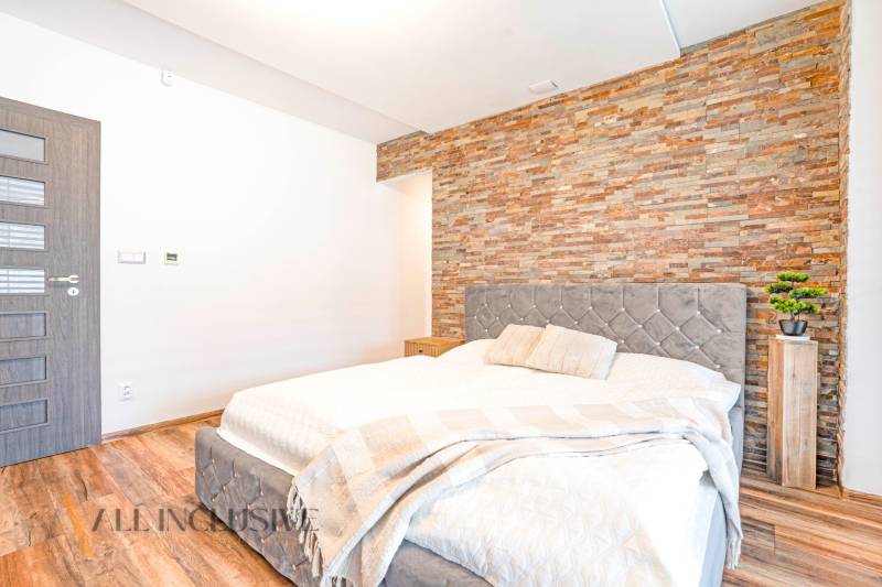 Ložnice v rodinném domě s kamennou stěnou, elegantní postelí a dekorativními doplňky.