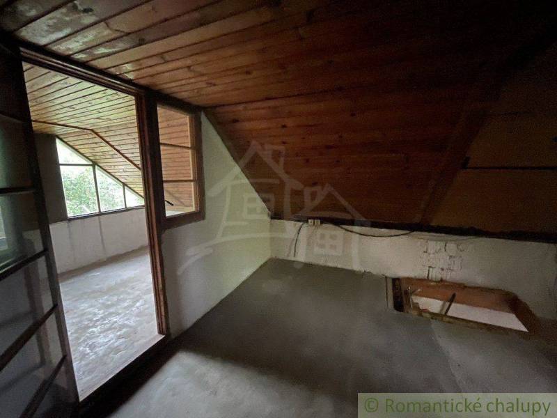 Podkrovní místnost s dřevěným obložením a prosklenou stěnou v rodinném domě.