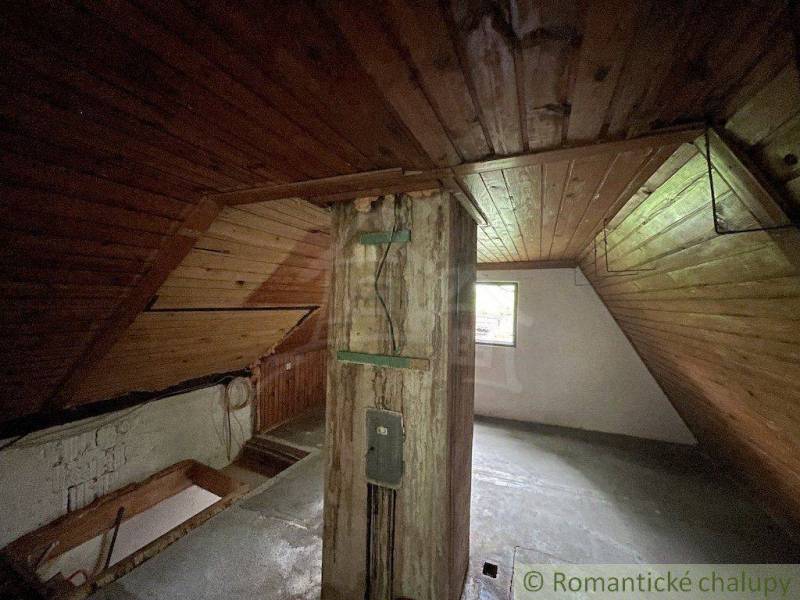 Podkroví v rodinném domě s dřevěným obkladem a trámem, prosvětlené oknem.