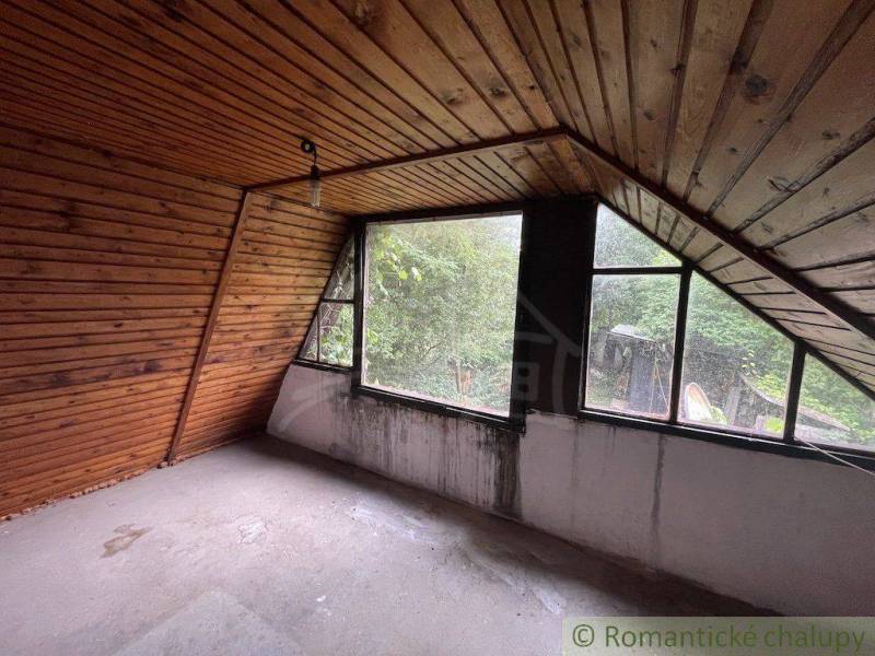 Podkrovní místnost v rodinném domě s dřevěným obkladem a velkými okny.