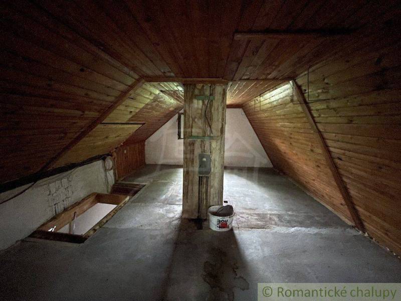 Podkroví s dřevěným obložením a betonovou podlahou v rodinném domě.