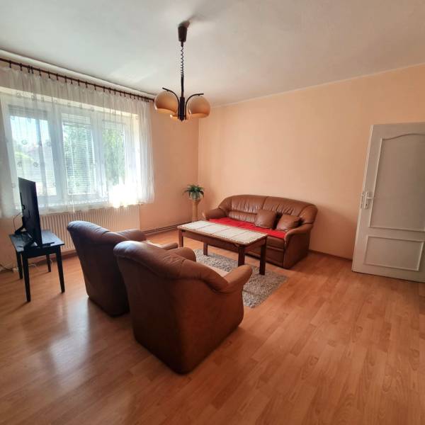 Obývací pokoj rodinného domu s pohovkou, křesly, televizí a dřevěným stolem na koberci.