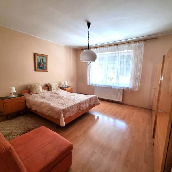 Ložnice v rodinném domě s manželskou postelí, obrazem a velkým oknem.