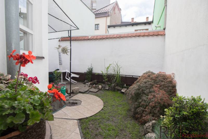 Malá zahrádka u 2pokojového bytu s dlažbou, rostlinami a dekorací z kamenů.