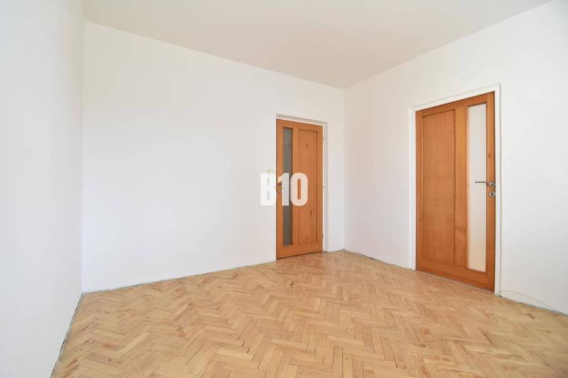 Bílé stěny a dřevěné parkety v místnosti 4pokojového bytu.
