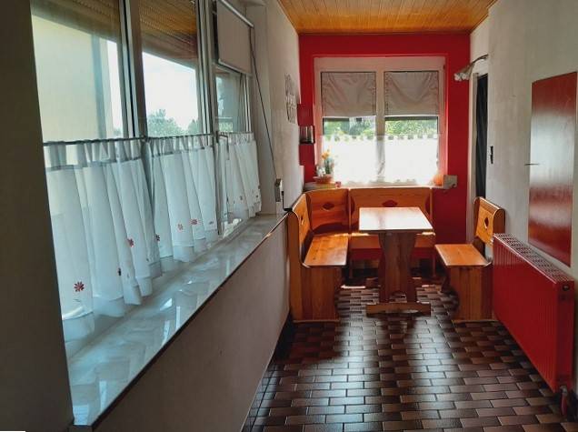 Rodinný dům s dřevěným posezením v kuchyni, červené stěny a kachličkovaná podlaha.