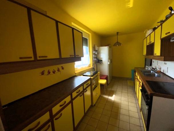 Kuchyně v rodinném domě se žlutými stěnami a skříňkami, prostor je světlý a funkční.