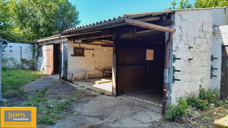 Plechová garáž s otevřenými dveřmi, obklopená zelení v Joise, Výstavba bytů.