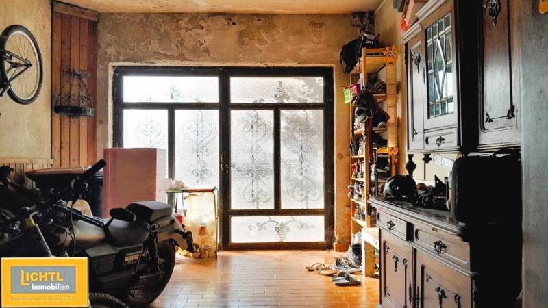 Garáž v rodinném domě, s motorkou, skříní a velkými prosklenými dveřmi.