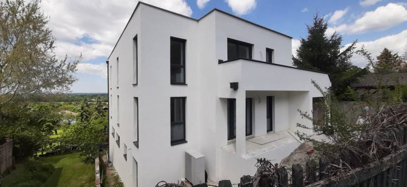 Vila v Hainburgu an der Donau s bílou fasádou, obklopená zelení a modrou oblohou.