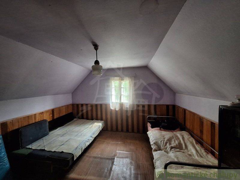 Interiér chaty se dvěma postelemi a dřevěným obložením, tlumené světlo.