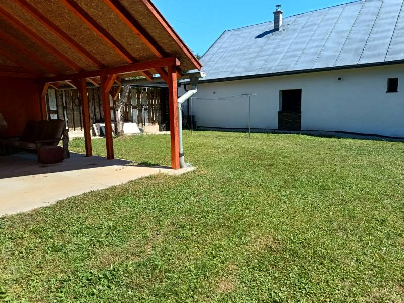 Zahrada u chaty v Tužině s přístřeškem a trávníkem na slunném místě.
