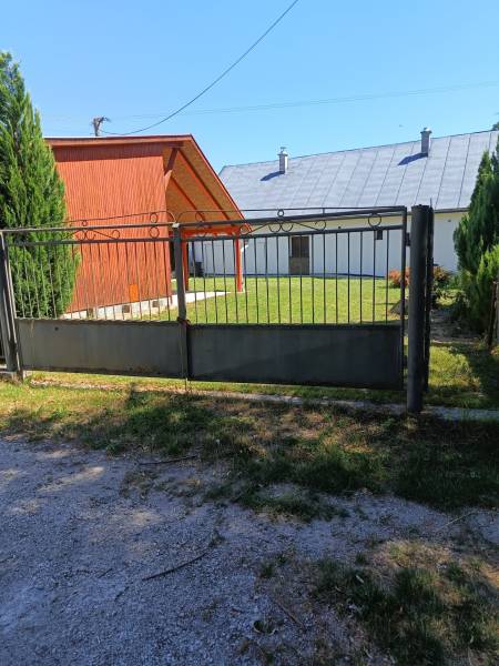 Brána a dřevěná chata v Tužině, obklopené trávníkem a jehličnany.