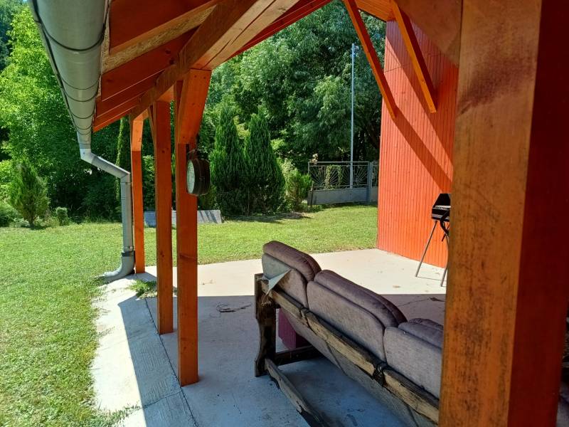 Veranda u chaty v Tužině s posezením a grilem obklopená zelení.