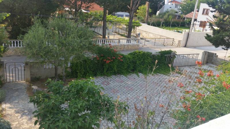 Zahrada rodinného domu ve Vrsi s dlažbou, zelení a květinami.