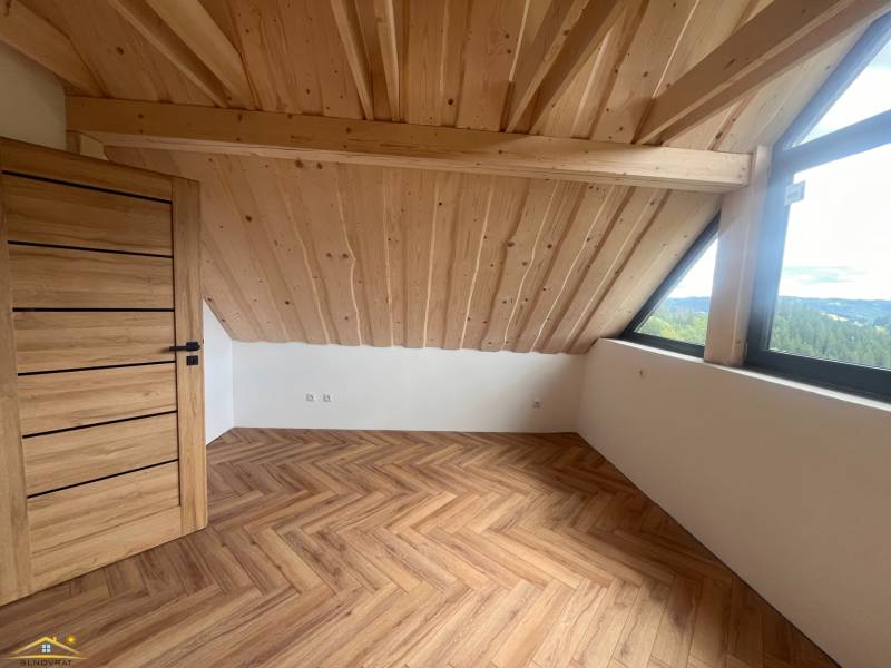 Podkrovní pokoj v chatě s dřevěným stropem, velkým oknem a parketovou podlahou.