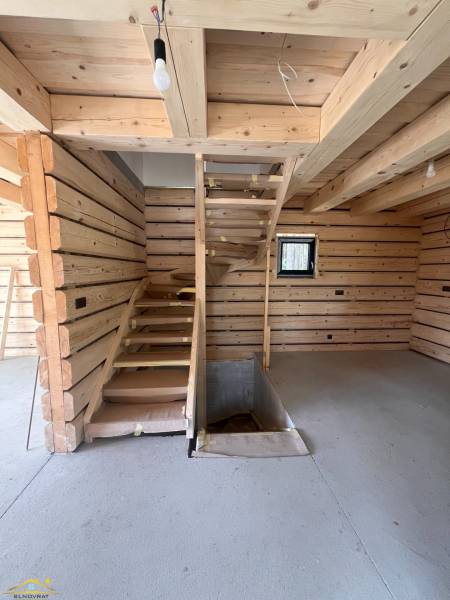 Dřevěný interiér chaty s betonovou podlahou a schodištěm.