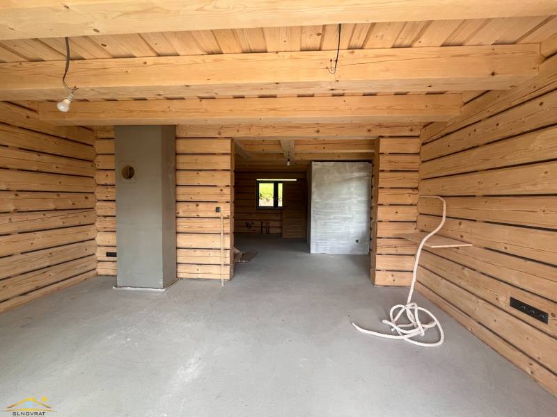 Dřevěný interiér chaty s betonovou podlahou a nedokončenými prvky.