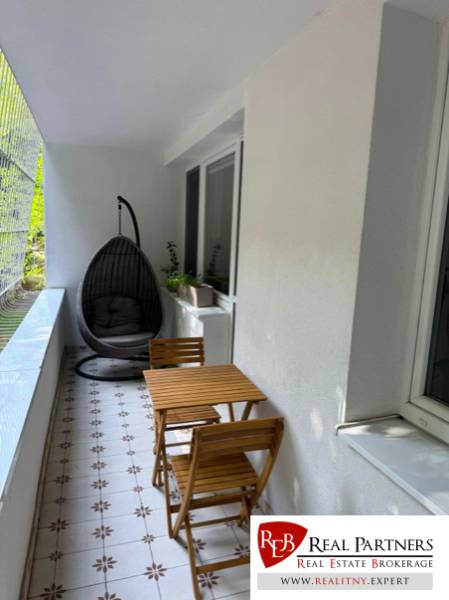 Zasklený balkon 4pokojového bytu s posezením a závěsným křeslem.