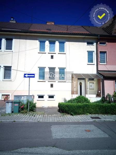 Rodinný dům v Novácích s bílou fasádou, zelenými keři a parkovištěm před domem.