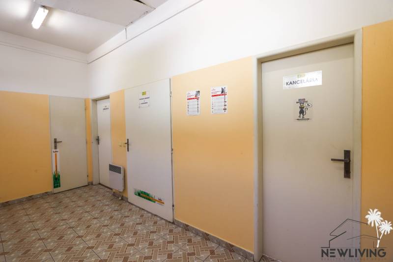 Chodba s dveřmi v obchodních prostorách, světlé stěny a dlažba na podlaze.