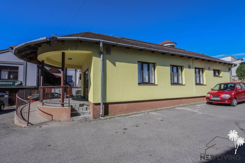 Žlutá budova s parkovištěm a autem na ulici Slovenského národního povstání ve Vrbovém.