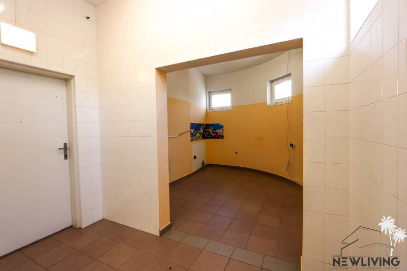 Obchodní prostory s bílými dlaždicemi, jasným osvětlením a oranžovými stěnami interiéru.
