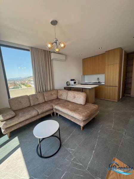 Obývací pokoj rekreačního apartmánu s rohovou sedačkou, výhledem a kuchyňským koutem.