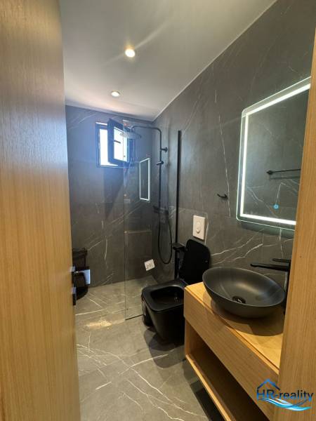 Koupelna rekreačního apartmánu se sprchovým koutem, černým umyvadlem a osvětleným zrcadlem.