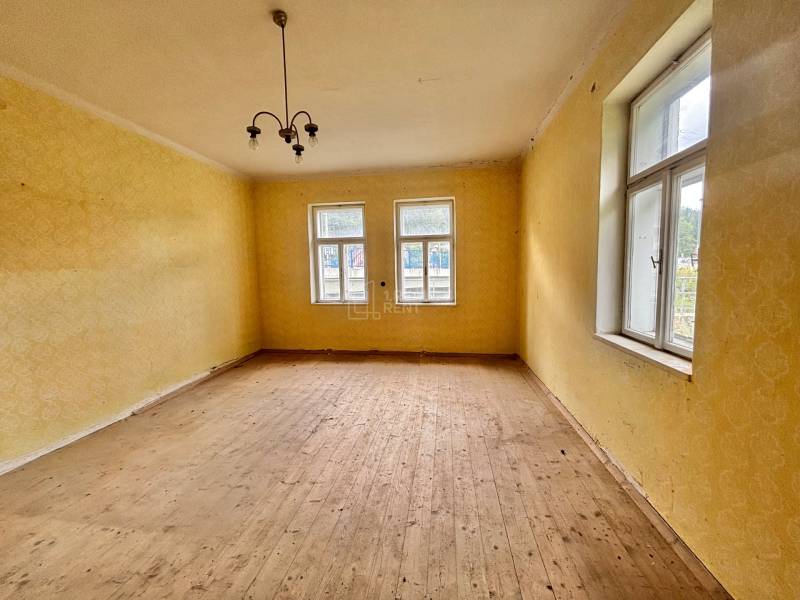 Pokoj v rodinném domě s dřevěnou podlahou, žlutými stěnami a závěsným svítidlem.