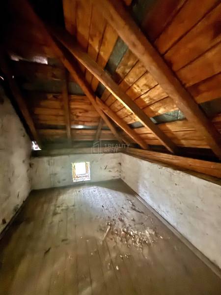 Podkrovní prostor v rodinném domě s dřevěným trámovým stropem a malým oknem.