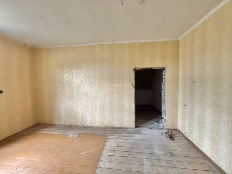 Pokoj v rodinném domě s dřevěnou podlahou a béžovými tapetami.