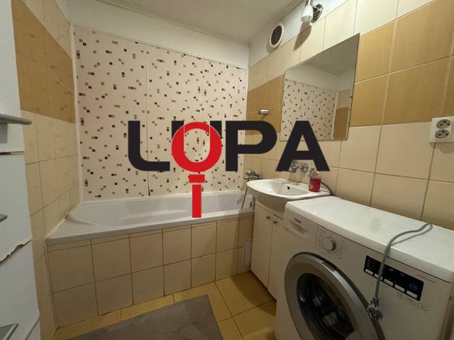 Koupelna v 3-pokojovém bytě s vanou, pračkou a obklady na stěnách.