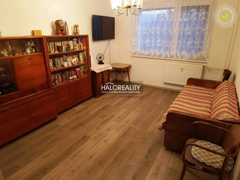Pěkný obývací prostor s pohovkou a knihovnou v 2-pokojovém bytě, dřevěná podlaha.