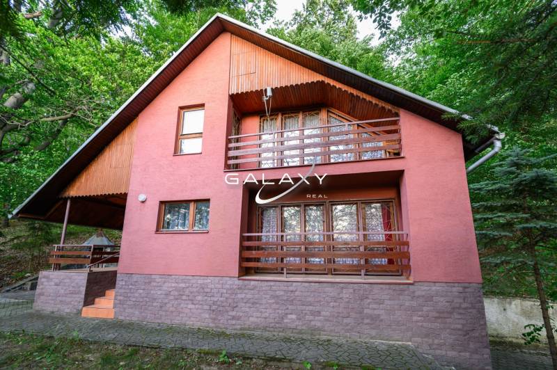 Dřevěná chata v Ružiné, obklopená zelení a s terasou v patře.