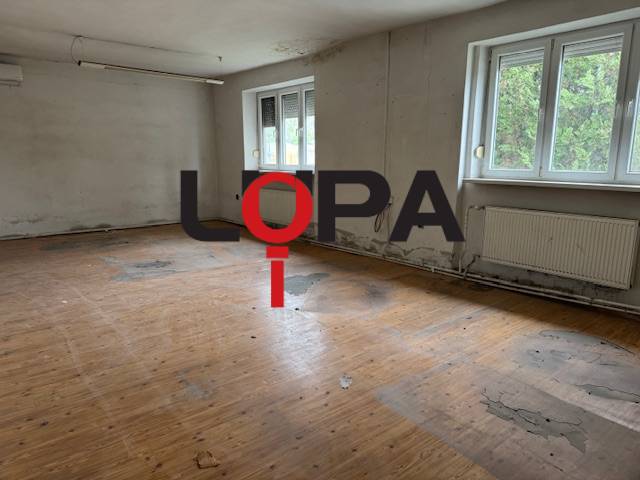 Opuštěná místnost v budově s dřevěnou podlahou a velkými okny.