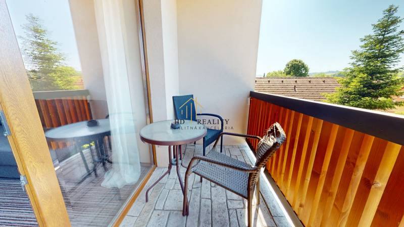 Balkon v 2-pokojovém bytě s výhledem na okolní zeleň a střechy.