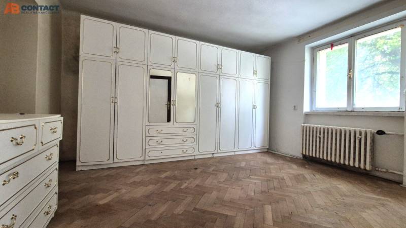 Pokoj třípokojového bytu s bílou vestavěnou skříní a dřevěnou podlahou.