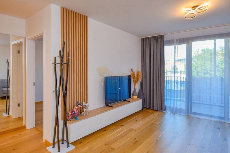 Obývací pokoj v 3pokojovém bytě s TV, proskleným balkonem a dřevěnou podlahou.