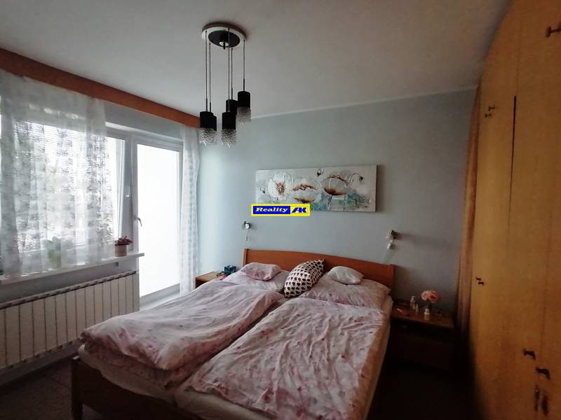 Ložnice v rodinném domě s manželskou postelí, skříní a balkónovými dveřmi.