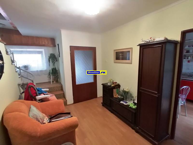 Obývací pokoj v rodinném domě s dřevěným nábytkem a schodištěm.