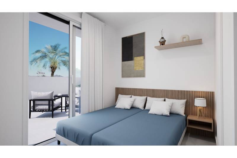 Ložnice rekreačního apartmánu s postelemi a přístupem na balkon s palmou.