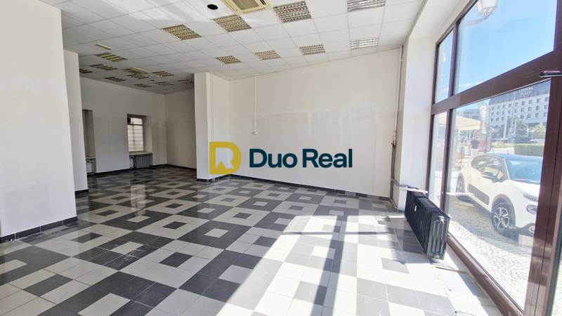 Obchodní prostory s velkými okny, dlažba a bílé stěny.